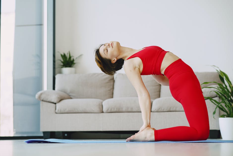 Side view of flexible sportswoman with closed eyes wearing red sportswear during home workout on sport mat on floor near sofa in modern apartment adhering to healthy lifestyle